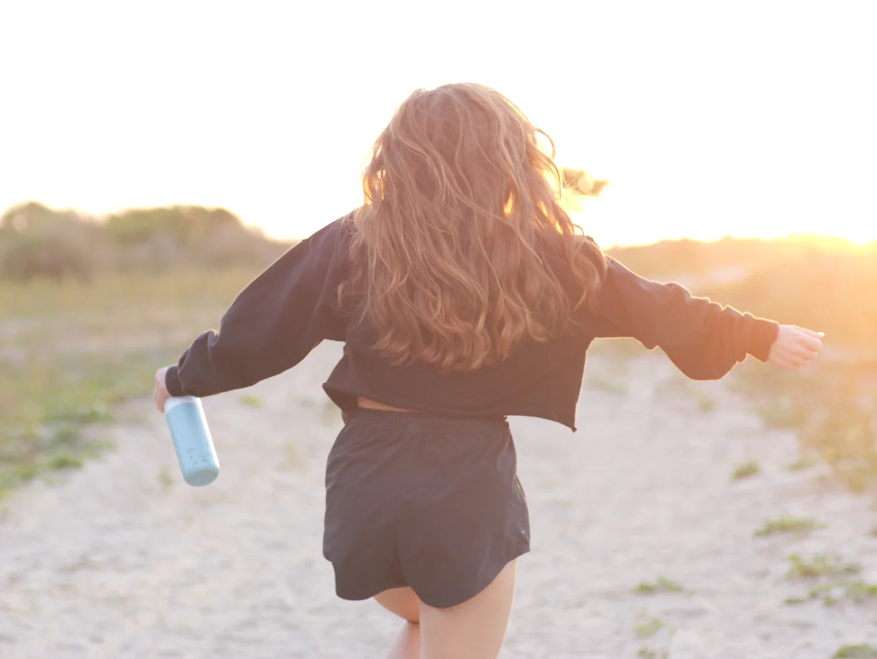 Een vrouw met uitgestrekte armen loopt het warme tegenlicht tegemoet