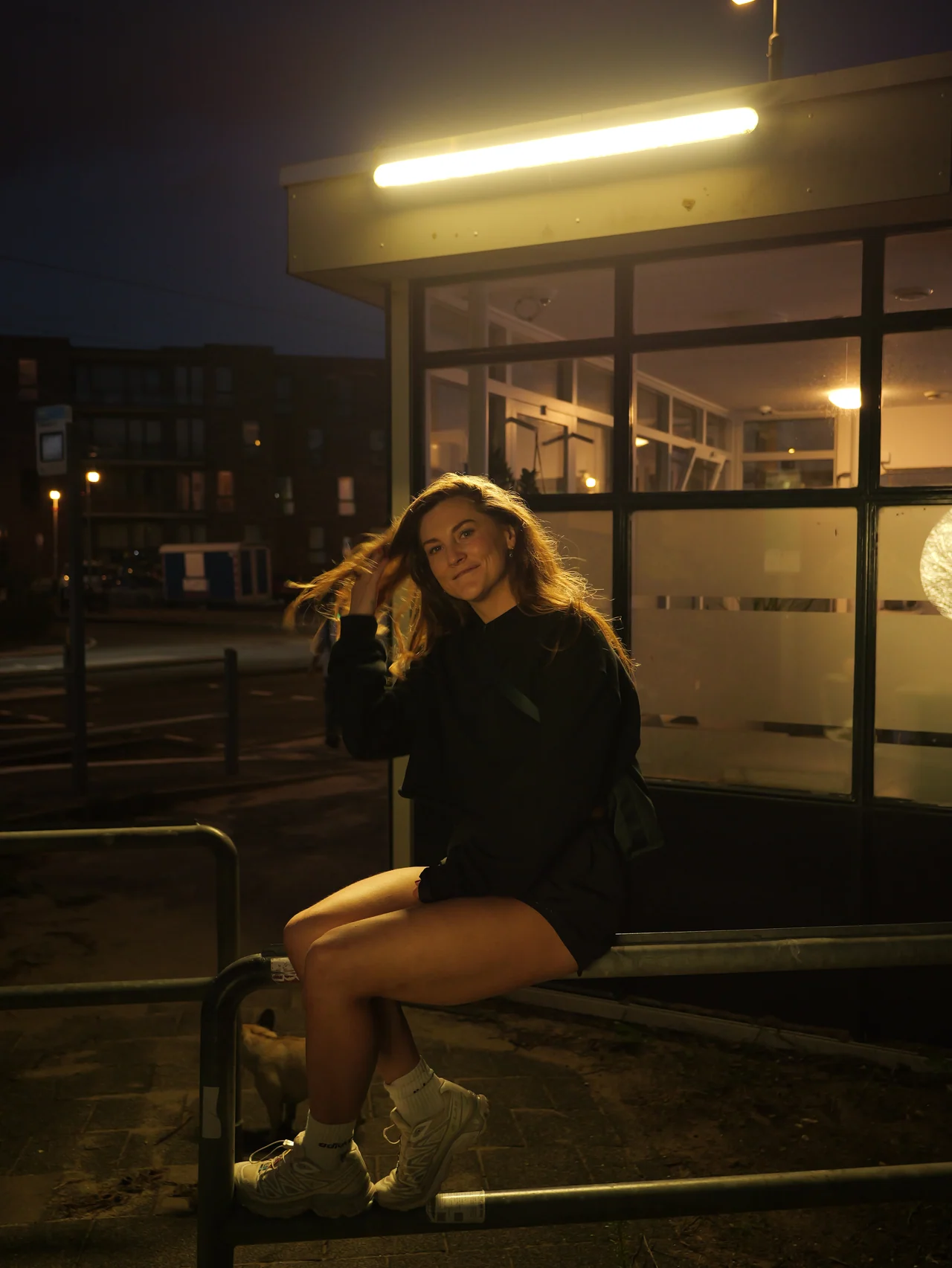 Een vrouw onder het warme gele licht van een halte in de nacht