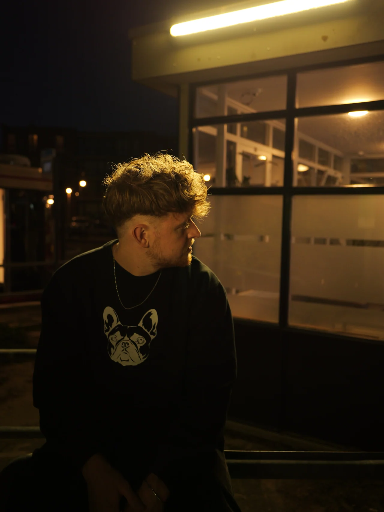 Een man in profiel naast een verlichte glazen gevel in de nacht
